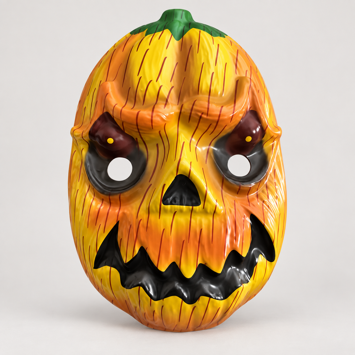 Masque citrouille Halloween effrayant orange et jaune avec yeux noirs, bouche monstrueuse et tige verte, sur fond blanc.